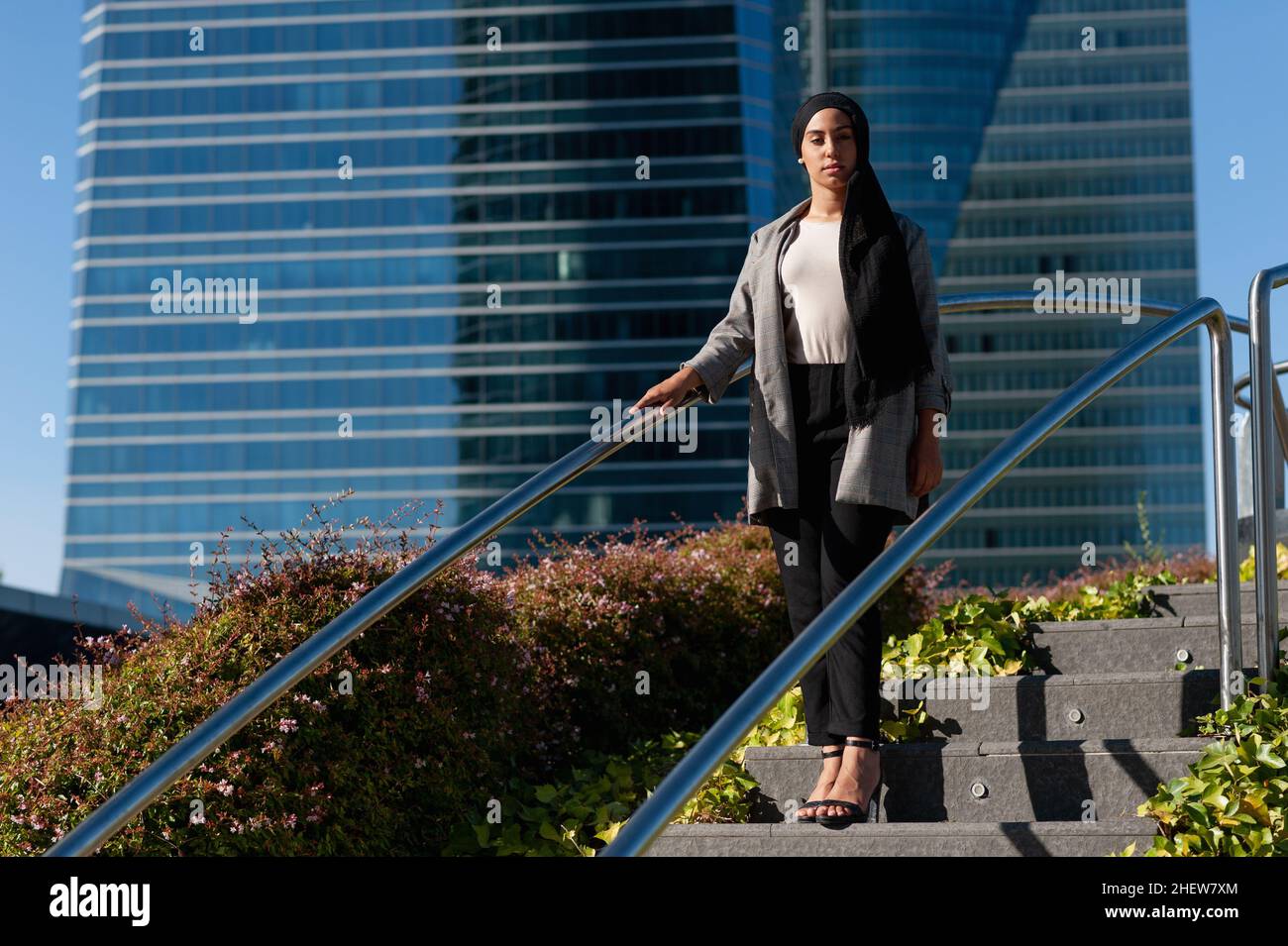 Unsmiling adult muslim woman standing on a step of a park staircase looking at camera in a sunny day. Stock Photo