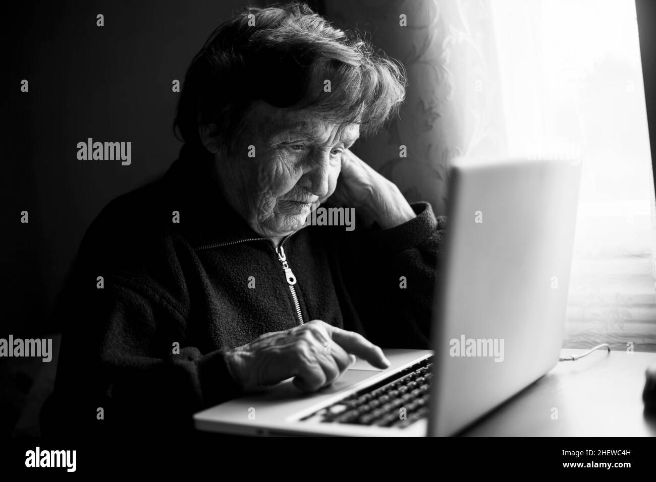 Elderly woman learns to work at her computer at home. Black and white photo. Stock Photo