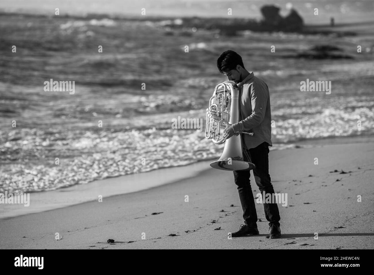 Musician with a tuba near the ocean shore. Black and white photo. Stock Photo
