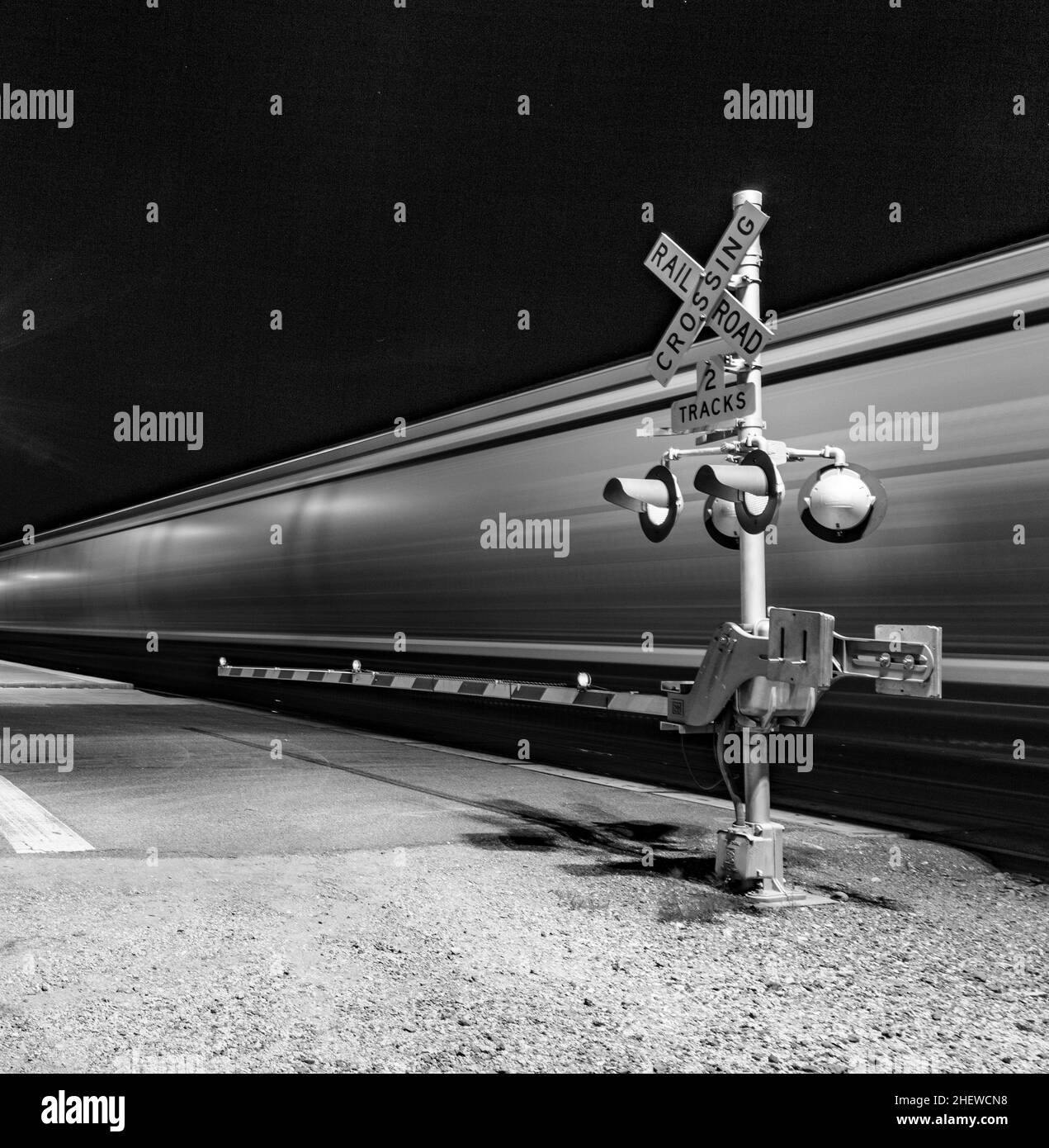 Railroad crossing with passing train by night Stock Photo