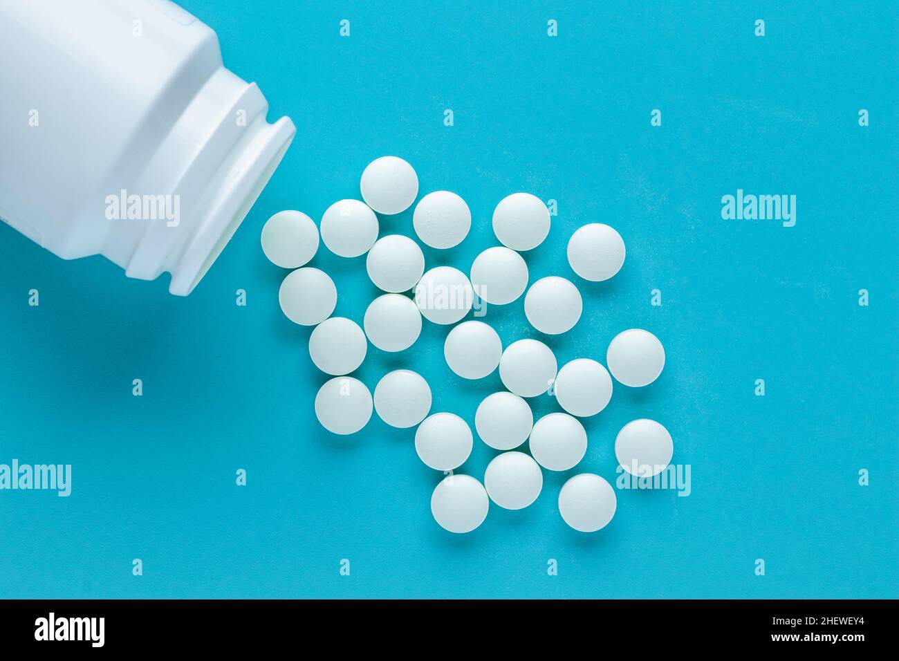White pills on a blue background, a bunch of scattered round tablets. Medicaments in bottle close-up. Overdose concept, disease treatment Stock Photo