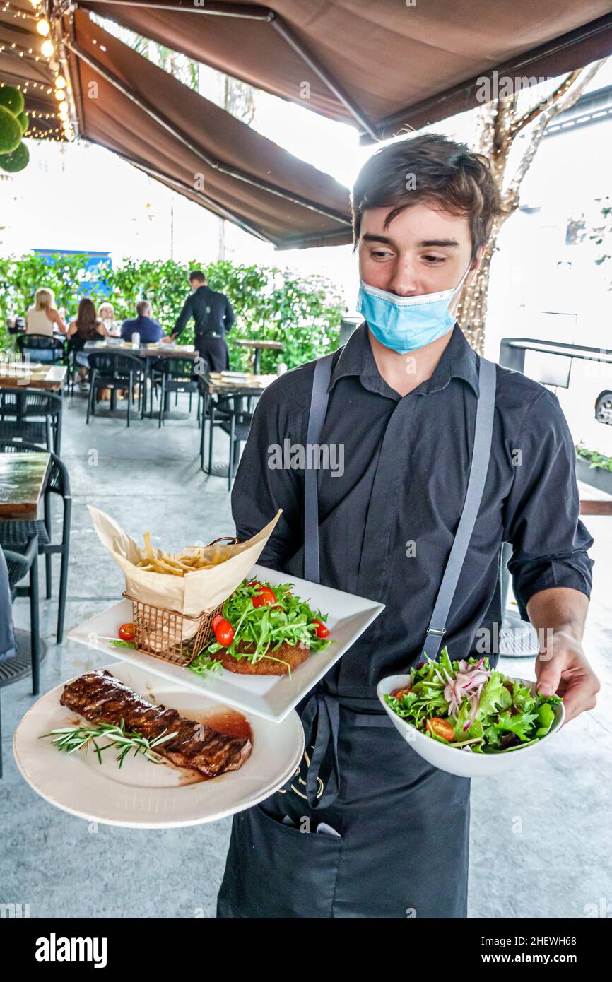 Miami Florida Brickell Baires Grill Argentinian restaurant Hispanic waiter server serving plates food wearing face mask Covid-19 pandemic Stock Photo