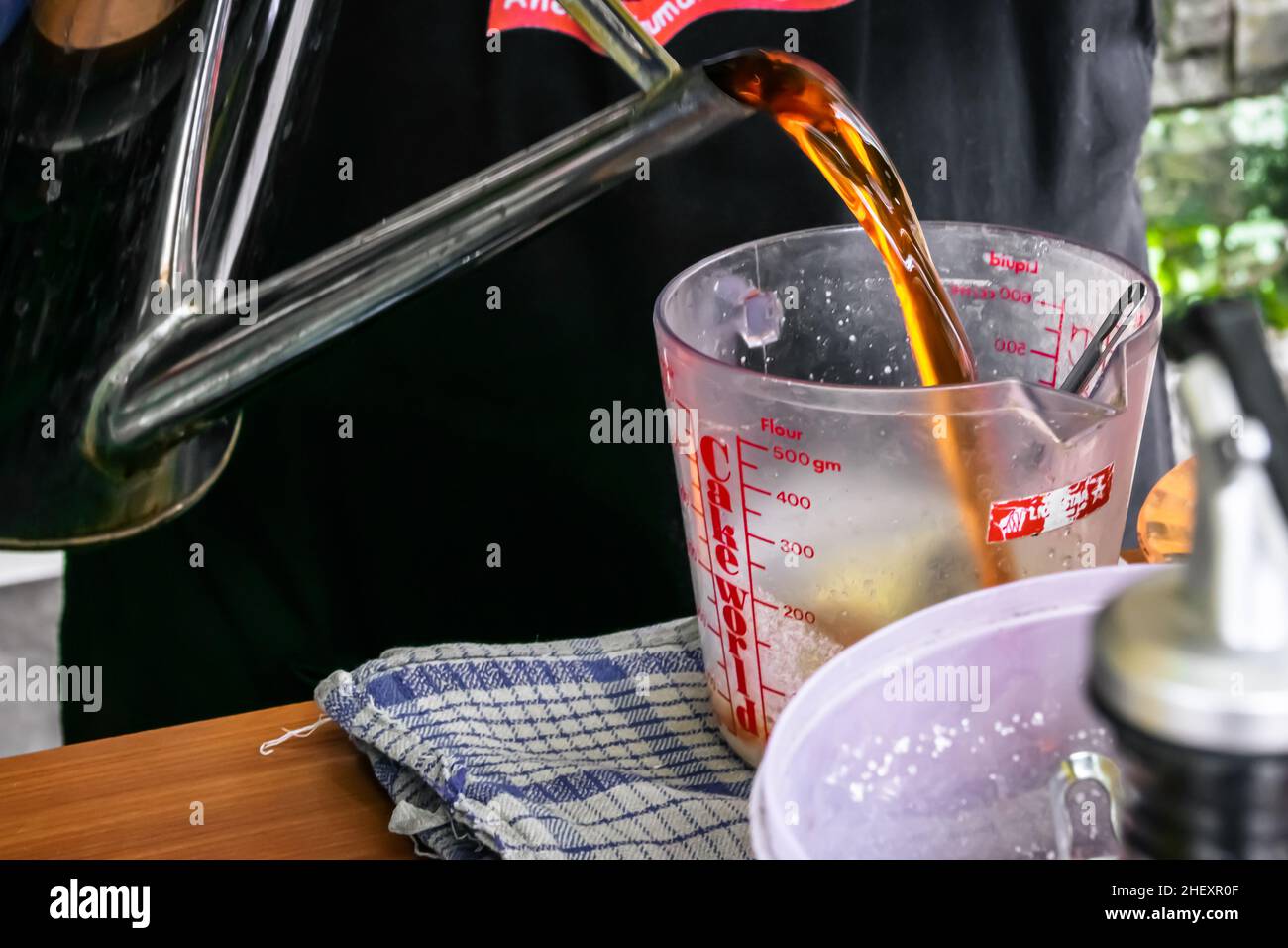 metallic chrome traditional vintage water jug or teapot pouring the brown tea into the measuring cup Stock Photo