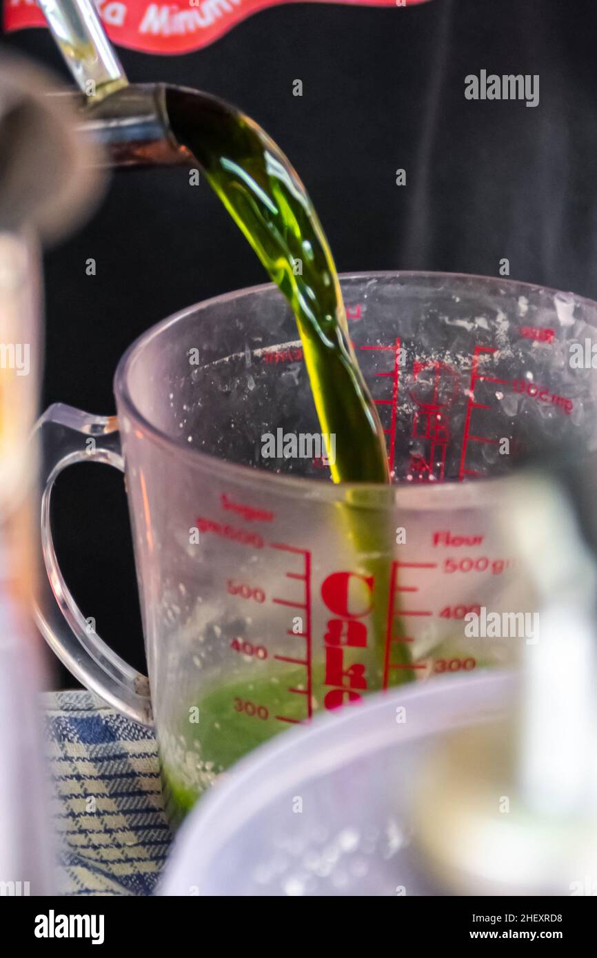 Close-up view of pouring a green tea or matcha water into a plastic transparent measuring cup for a thai tea with blurry and soft focus background Stock Photo