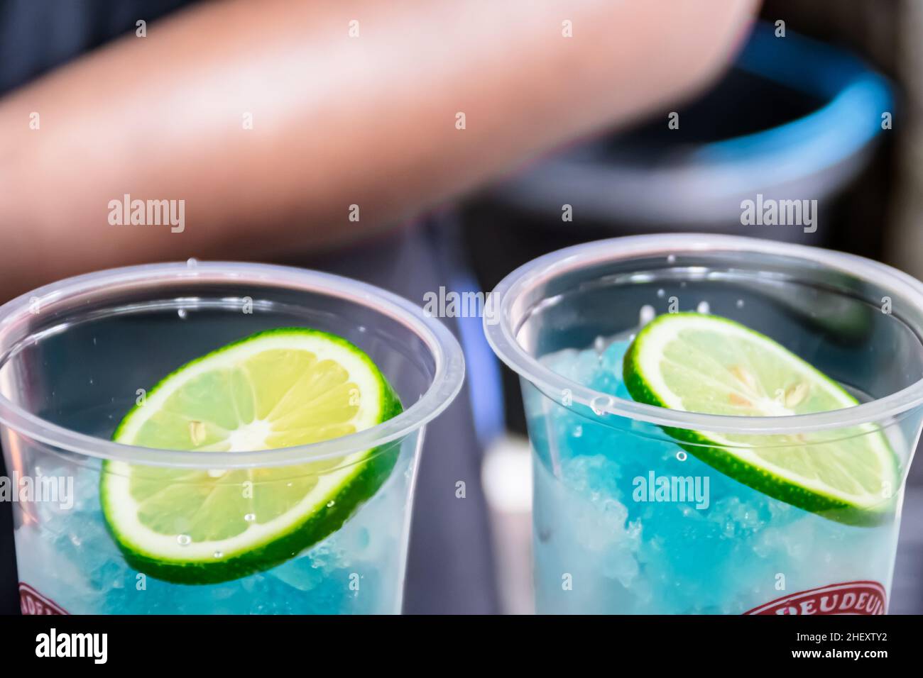 cold shaved ice with poured blue syrup and fresh sour limes sliced on top for a mojito drink in transparent plastic glass Stock Photo