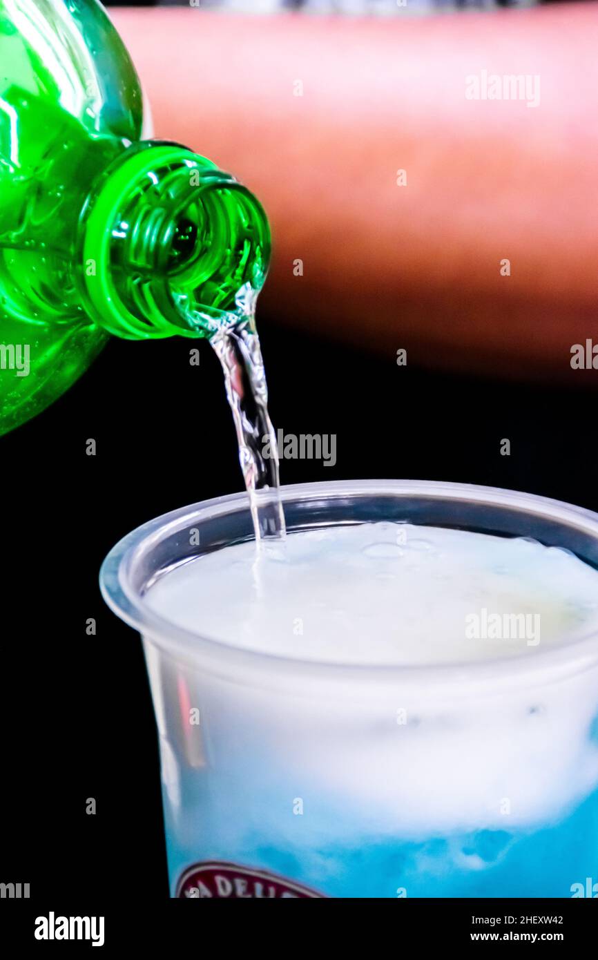 Pouring a soda water into a transparent plastic glass with cold shaved ice inside and and fresh sour limes sliced on top for a mojito drink for with a Stock Photo