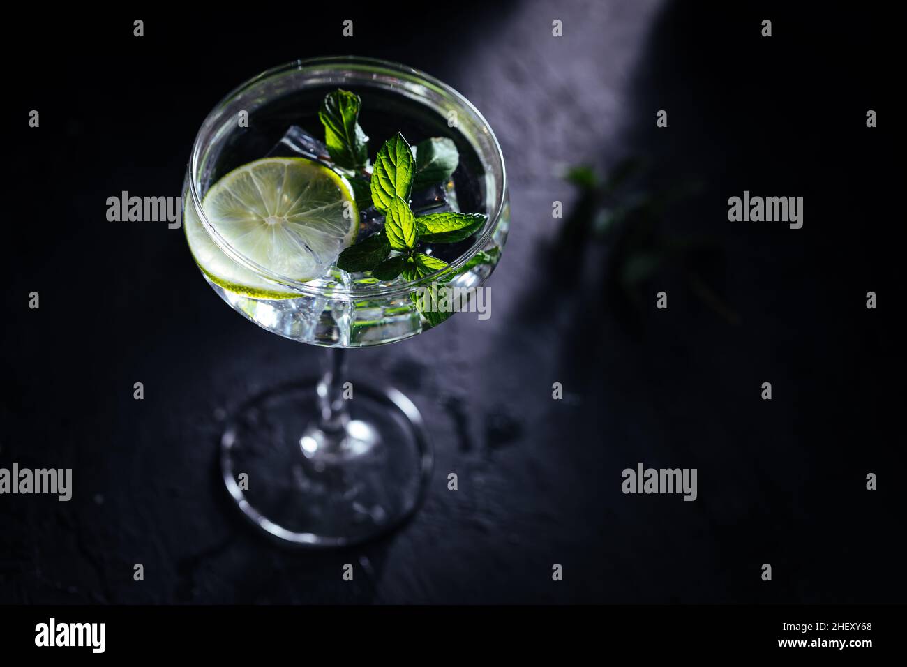 Gin tonic in cocktail glass with ice, mint leaves and lime on a dark rustic board Stock Photo