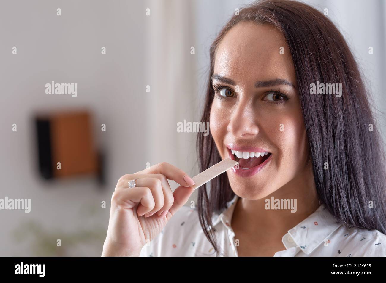 Good-looking brunette puts a chewing gum into her mouth looking into the camera. Stock Photo