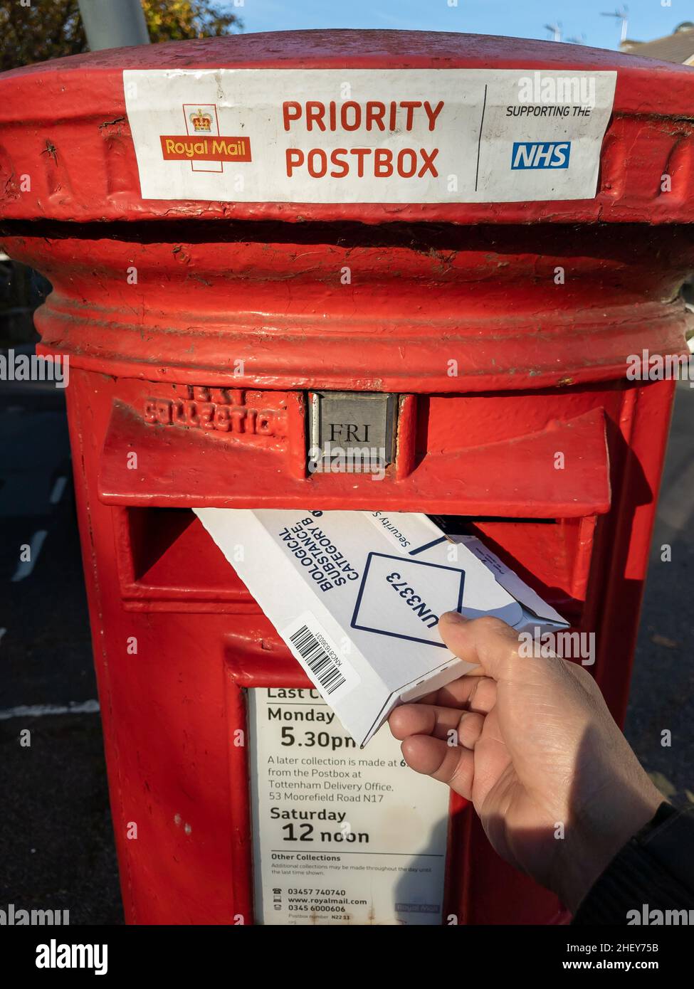 London.UK- 11.05.2021. A Royal Mail Priority Post Box with a person posting a Covid-19 test package. Stock Photo