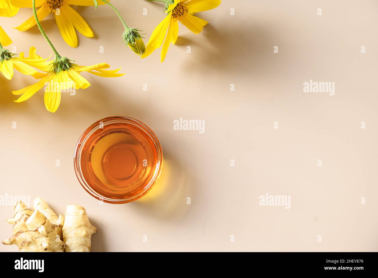 Jerusalem artichoke syrup in bowl, flowers and root on beige background
