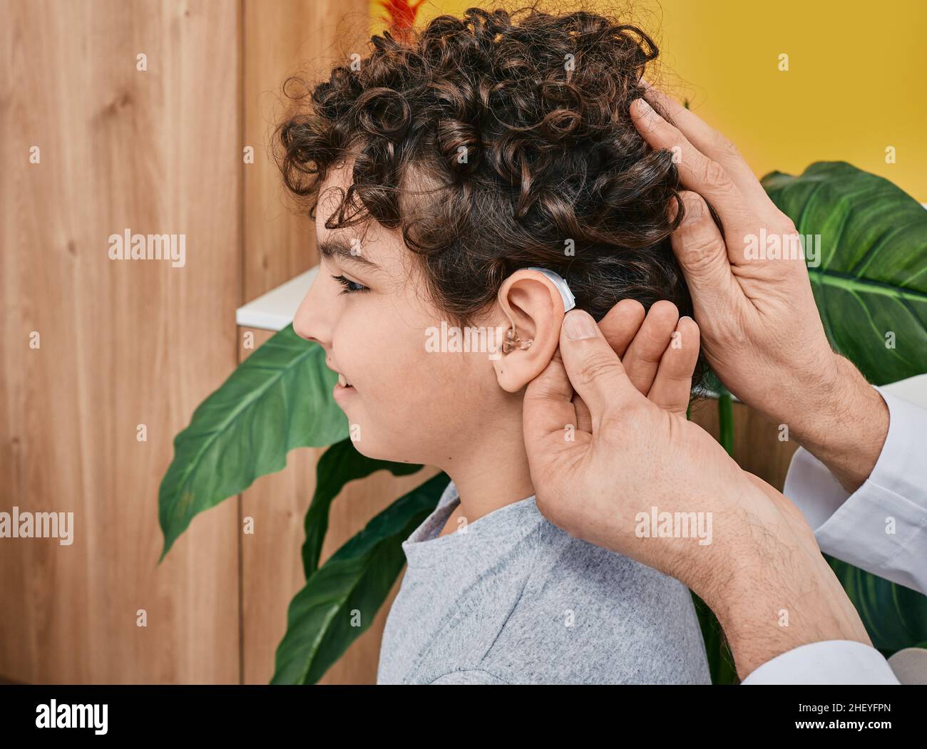 Hearing solutions for children. Audiologist fits a hearing aid on male child ear while visit a hearing clinic Stock Photo