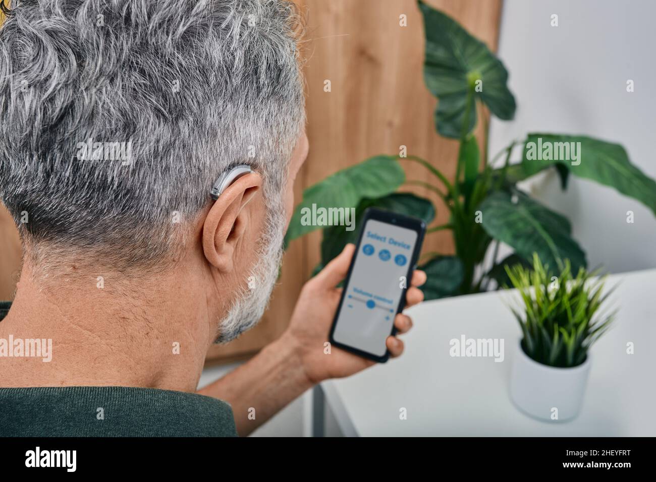 Hearing impaired mature man adjusts settings for his BTE hearing aid