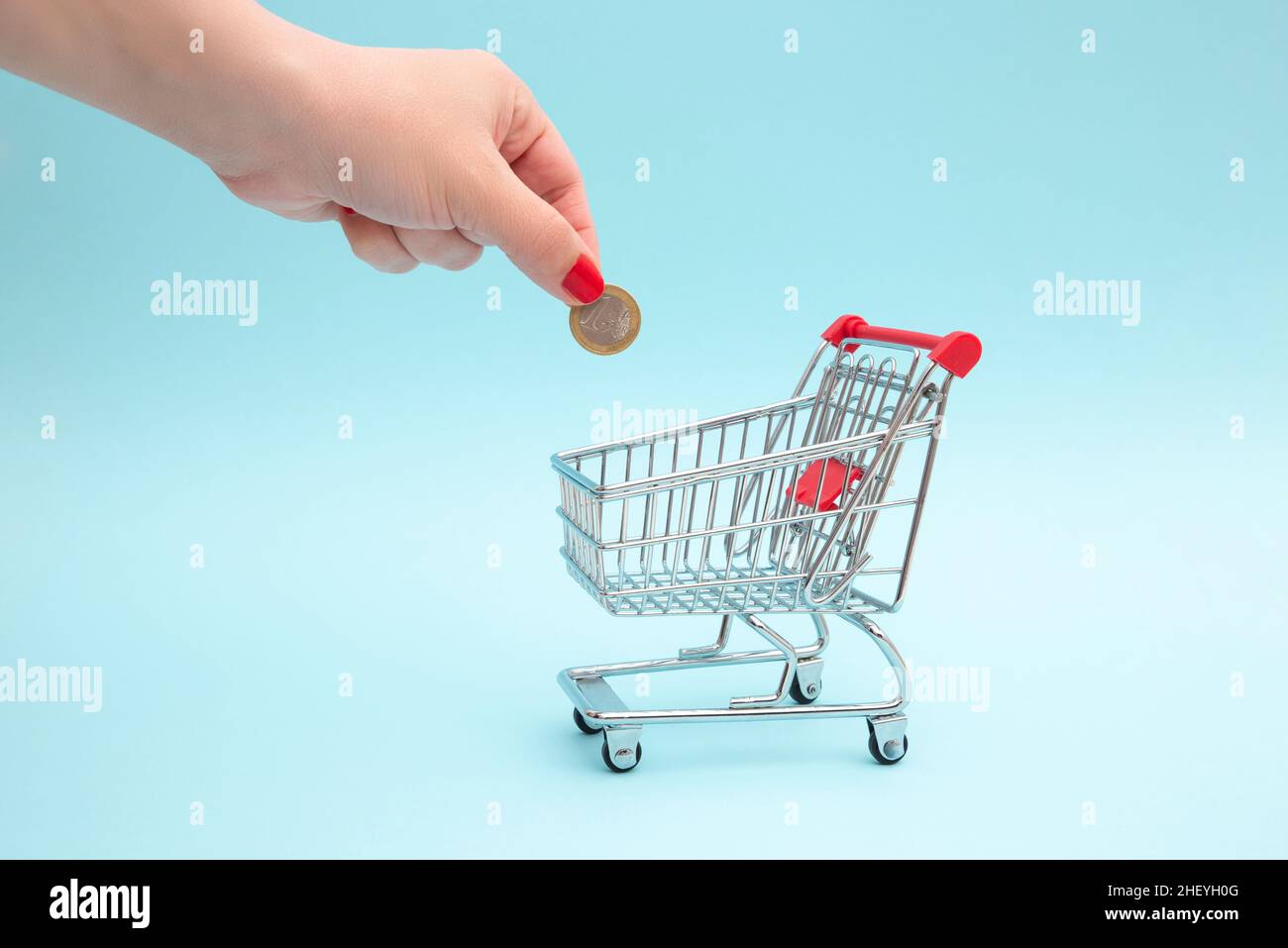 The hand puts a coin in the shopping cart. The concept of saving in stores and everyday grocery shopping Stock Photo