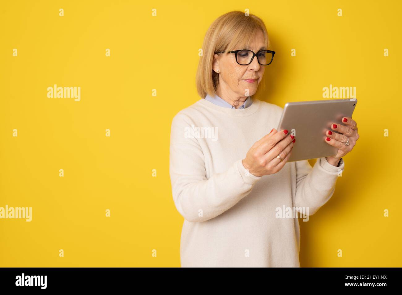 Senior woman using tablet isolated on yellow background Stock Photo