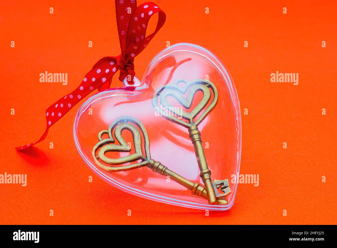Two retro style skeleton keys in a clear heart shaped box with a red dotted ribbon bow on a red background. The concept of openness and clarity for a Stock Photo