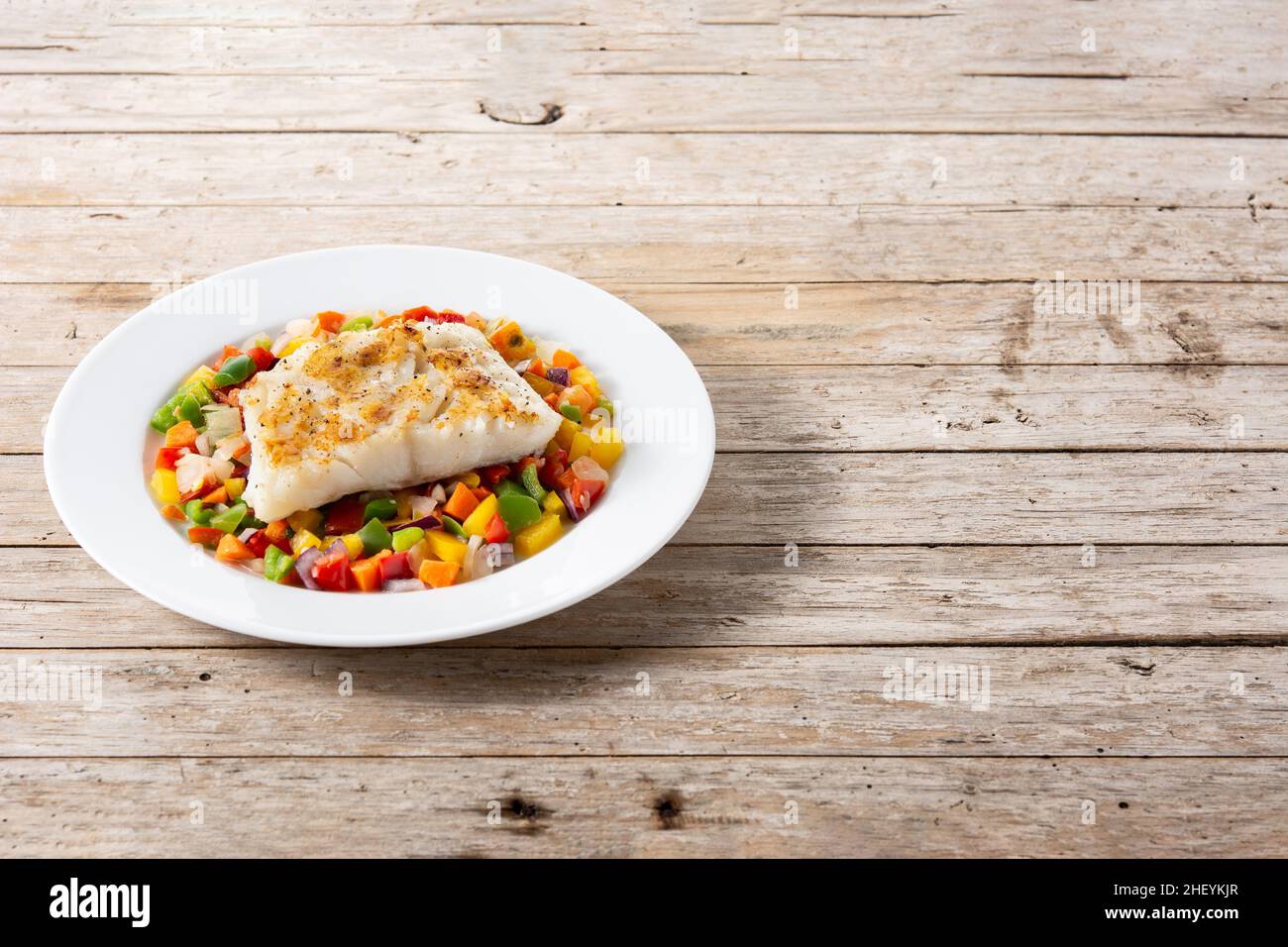 Grilled cod with vegetables in plate on wooden table Stock Photo