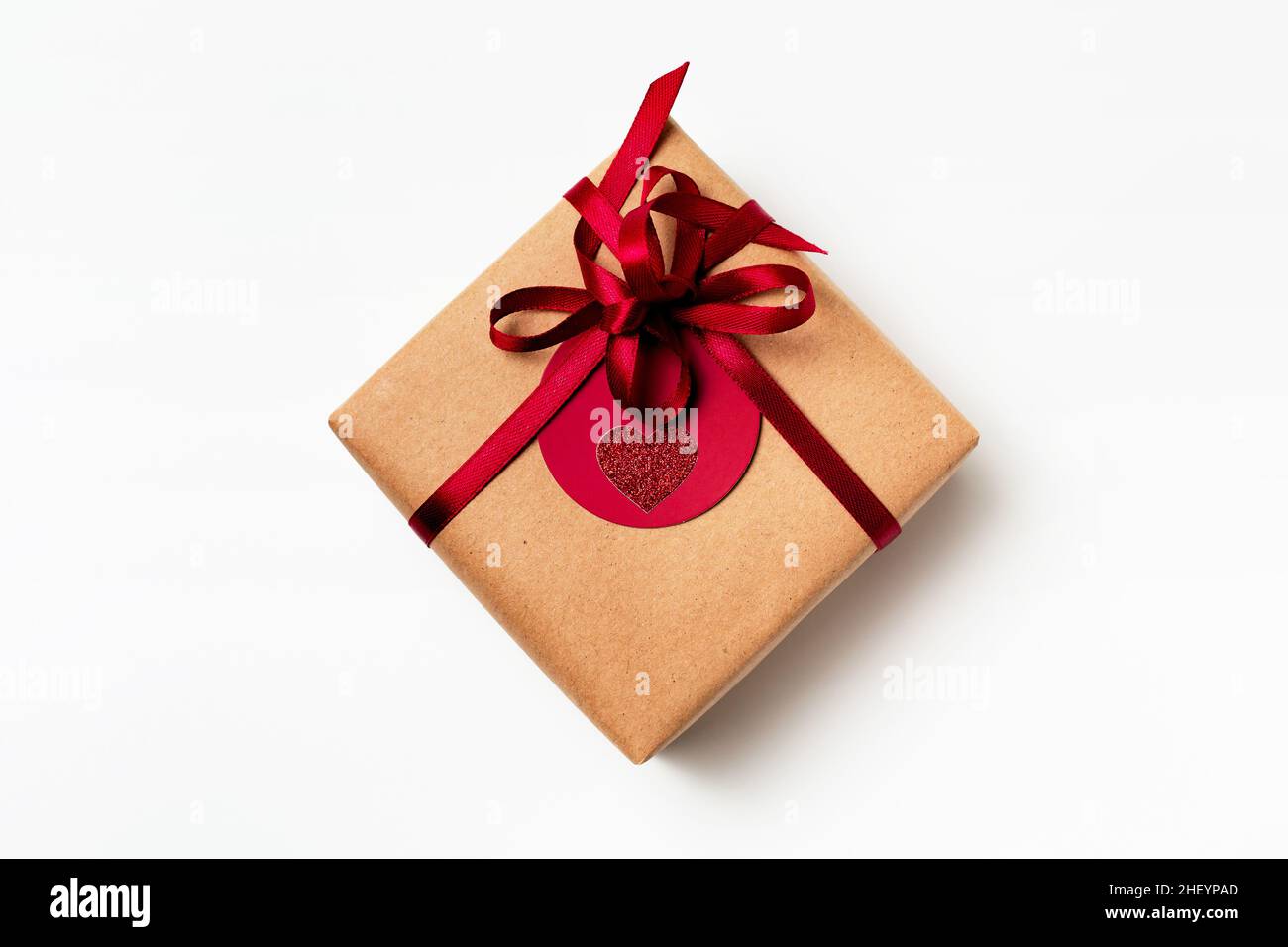 Elegant design of present gift box wrapped in brown craft paper with red ribbon and red tag, top view on white background Stock Photo