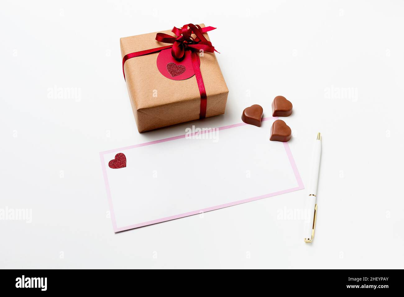 Romantic present gift box, white blank greeting card with pen and heart-shaped chocolate candies on white background Stock Photo