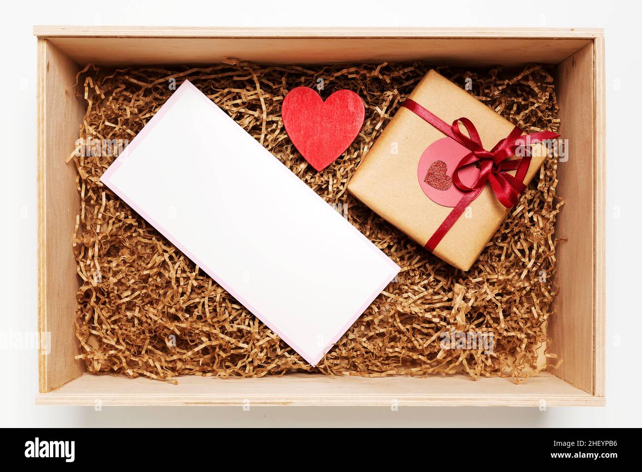 Wooden box with present wrapped in brown craft paper with red ribbon and empty blank card, top view from above Stock Photo