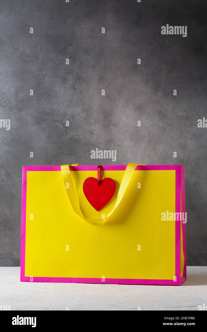 Valentines day present gift bag in bright colors pink and yellow with red heart-shaped tag, mockup Stock Photo