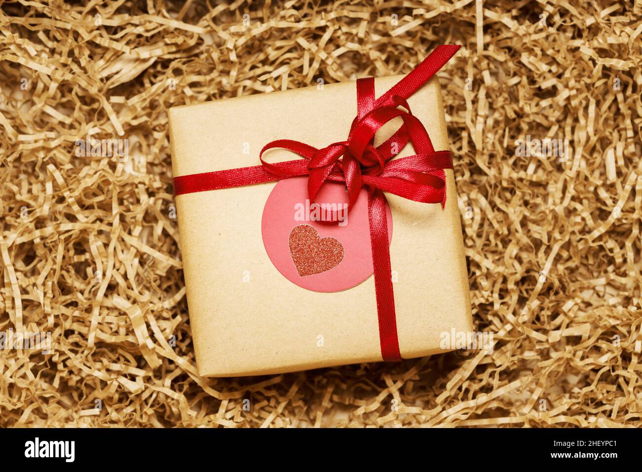 Present box wrapped in brown craft paper with red ribbon, filled with paper filler, top view from above Stock Photo