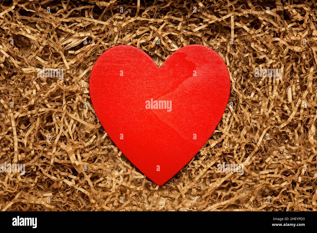 Present box with big red heart lying on brown shredded craft paper filler, top view from above, Valentine day concept Stock Photo