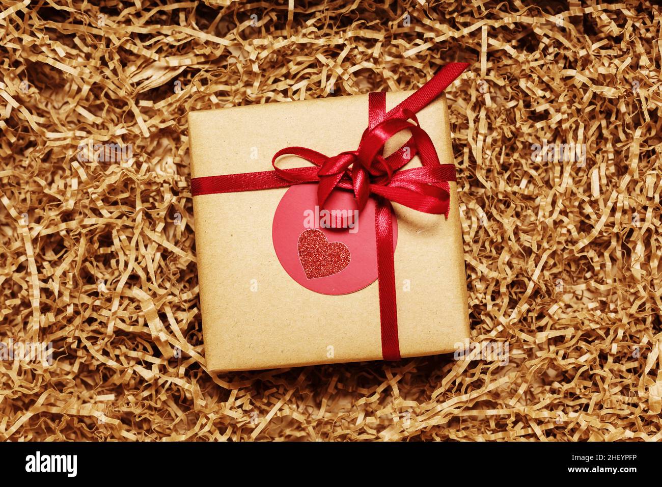 Present box wrapped in brown craft paper with red ribbon, filled with paper filler, top view from above Stock Photo