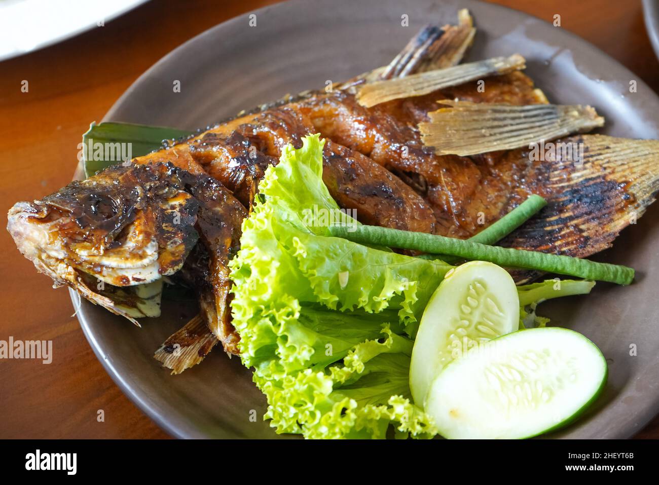 Grilled carp in soy sauce with fresh green vegetables and cucumber on a brown plate in a restaurant. Stock Photo