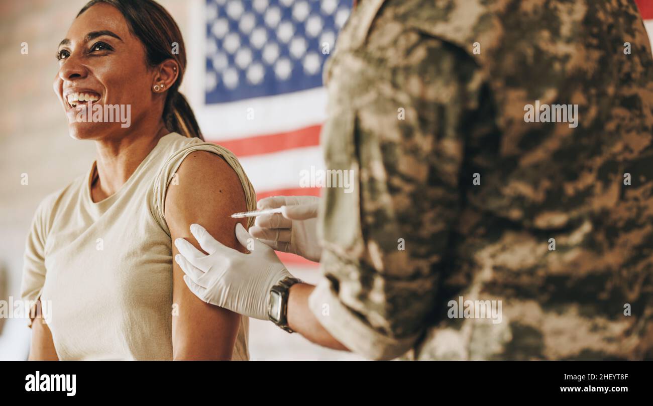 Servicewoman receiving a dose of the covid-19 vaccine in her arm. American soldier smiling happily while getting inoculated against coronavirus diseas Stock Photo