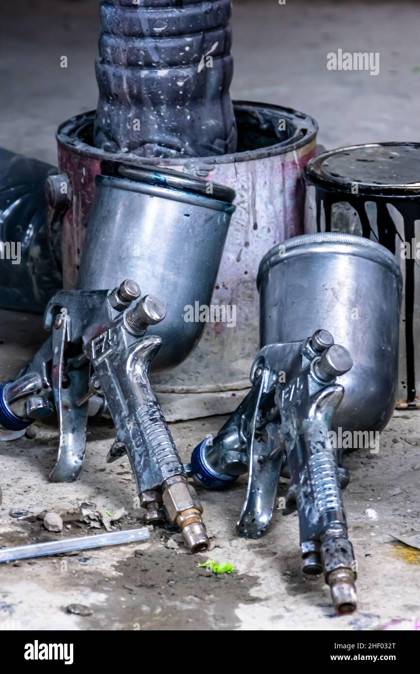 two metal industrial paint spray gun with the can behind for paintwork garage background Stock Photo