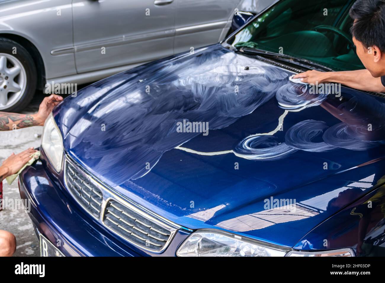 two mans rub and polish blue car or engine hood with hand to get