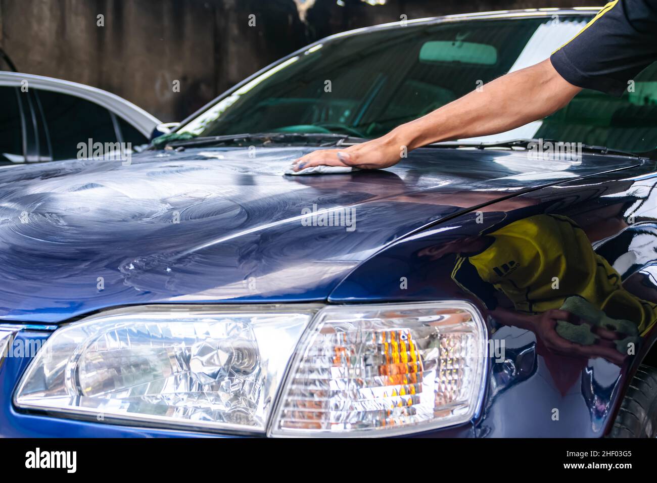 Man rub and polish blue car or engine hood with hand to get clean , shine and gloss at