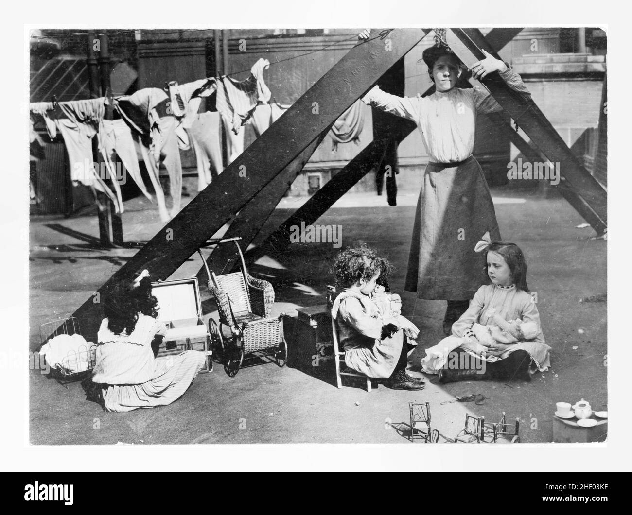 Living on a skyscraper. 3 girls playing with dolls, and woman standing in front of clothes on clothesline, on roof of a skyscraper, New York. 1919. Stock Photo