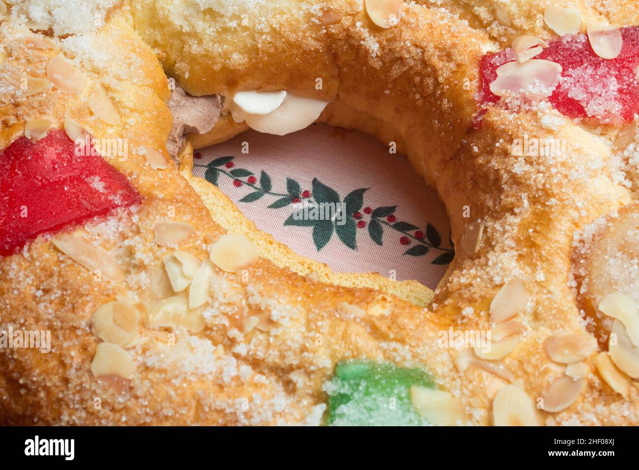 Decorated tablecloth with a draw of holly on Christmas Day in the middle of a large donut cake filled with whipped cream and decorated with red and gr Stock Photo