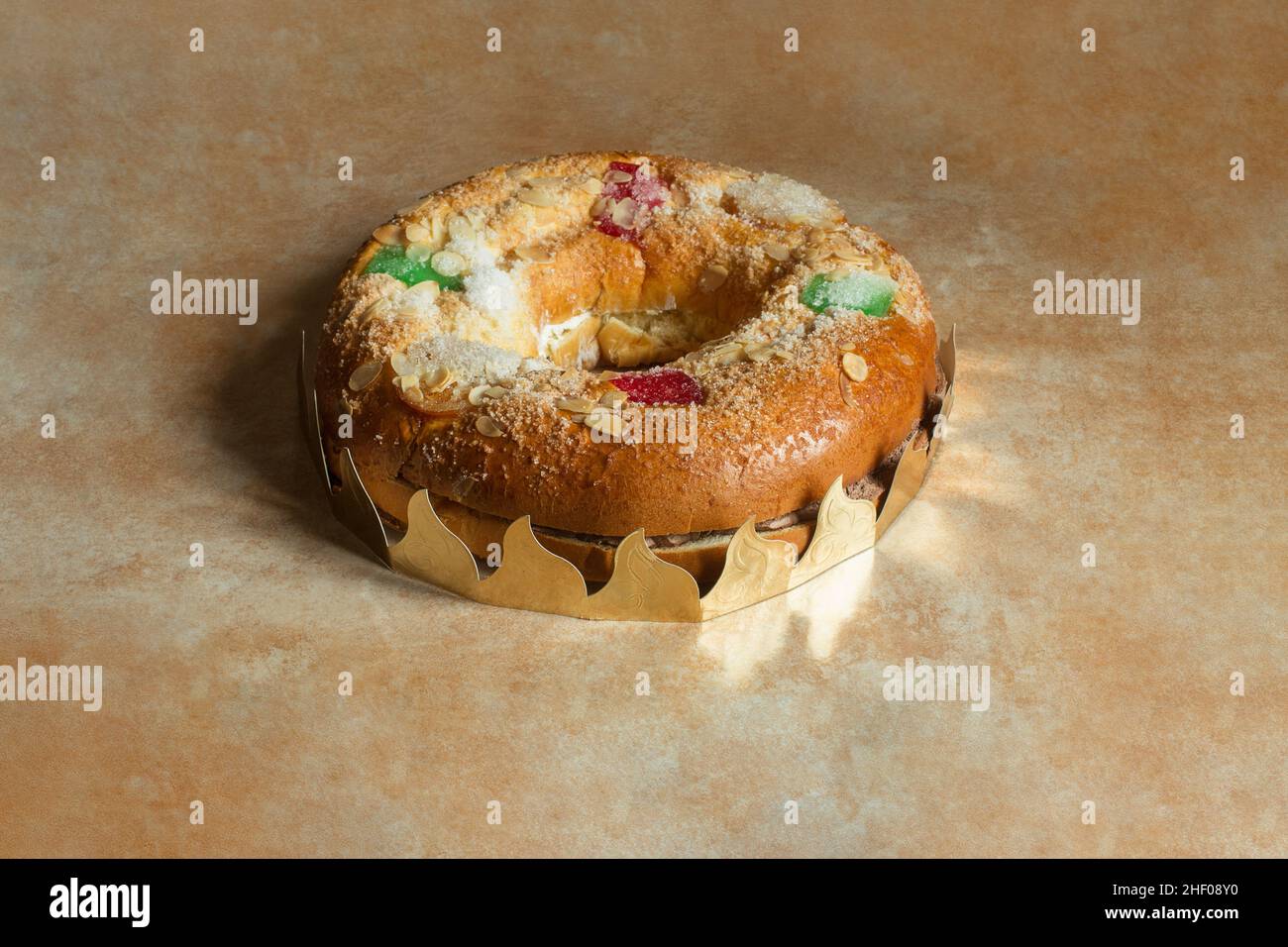 Large donut cake filled with sweet whipped cream and meringue with candied fruit, almonds, sugar, surrounded by a wreath on a textured abstract design Stock Photo