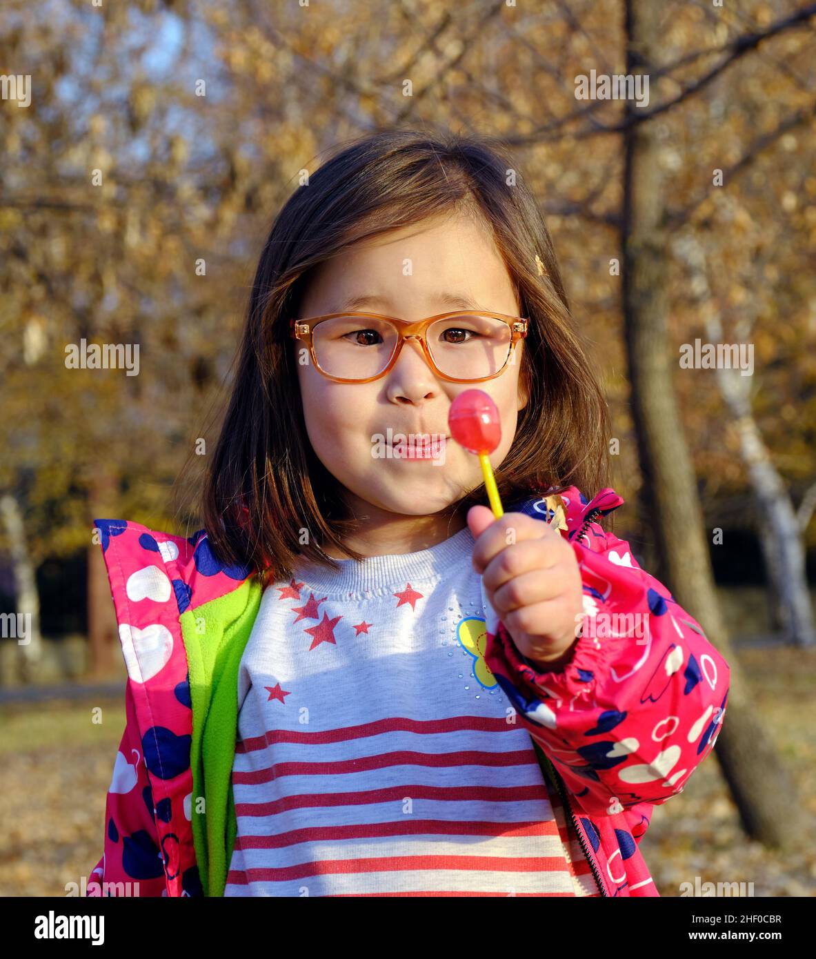 Almaty, Kazakhstan - October 22, 2020: cute girl in trendy clothes looking at lollipop candy Stock Photo