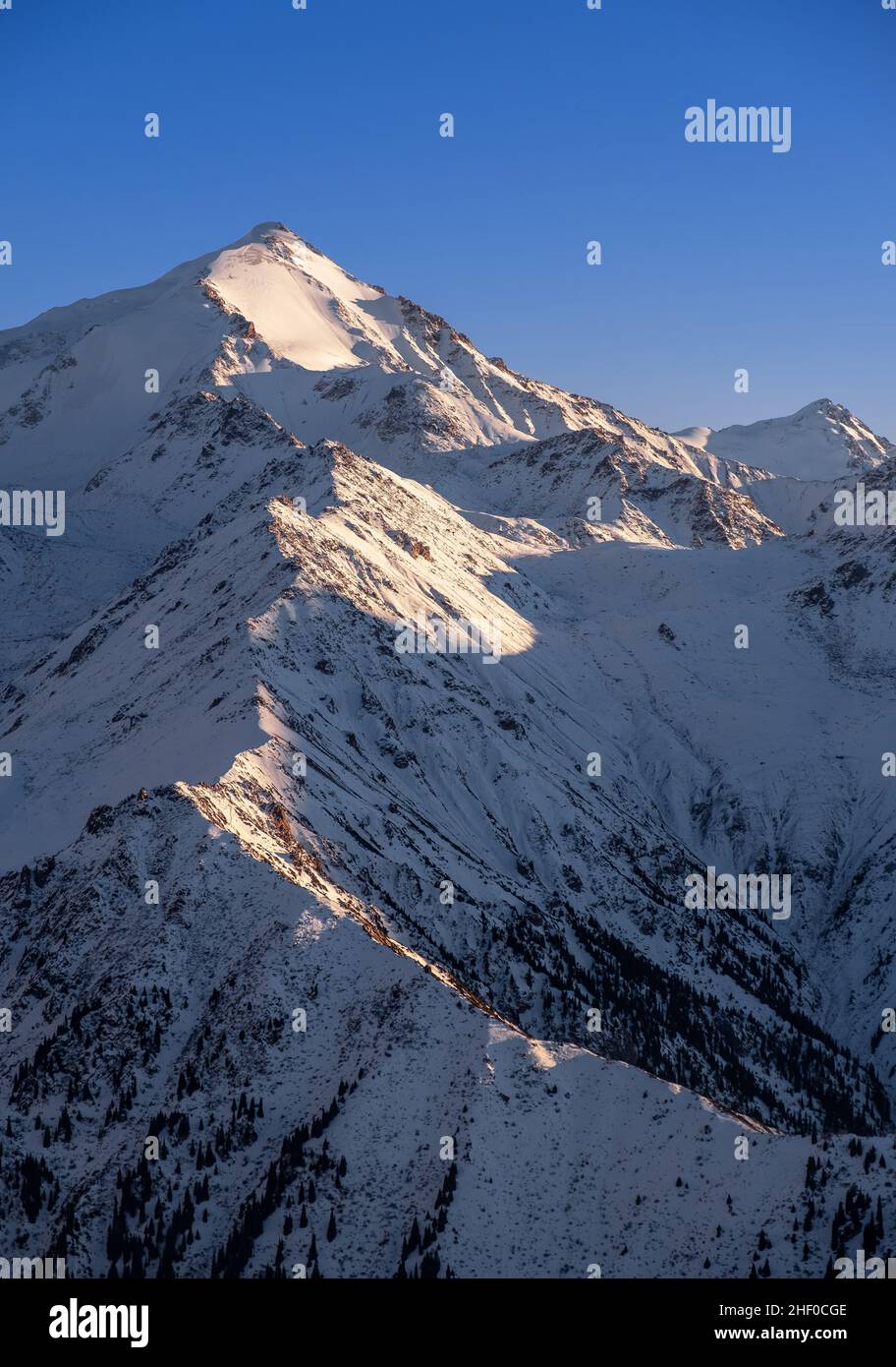 Snow-capped mountains at evening time before the sunset; majestic mountain peak on the background of blue sky in winter time Stock Photo