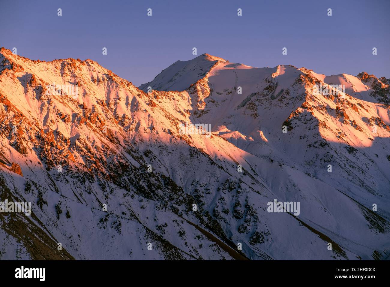 Soft evening sunlight on mountain ridges; rocky mountains covered with snow at sunset Stock Photo