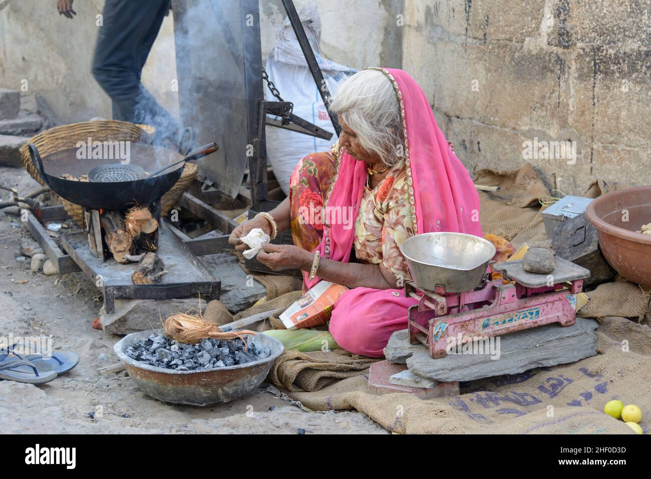 An elderly local Indian woman wearing a pink sari cooks street food on