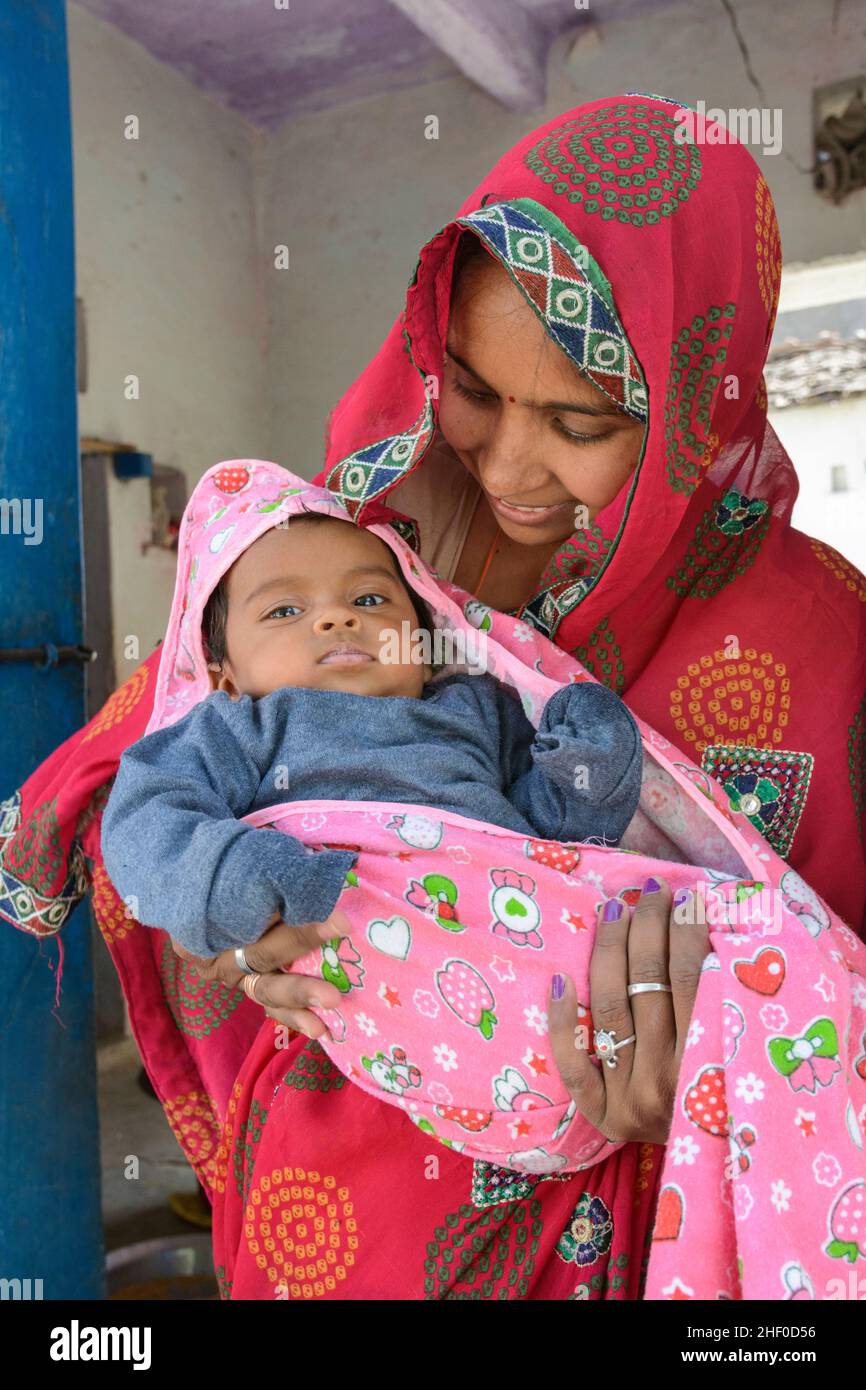 A local young Indian mother wearing a pink sari cradles her baby in her home in Nagda village, near Udaipur, Rajasthan, India, South Asia Stock Photo