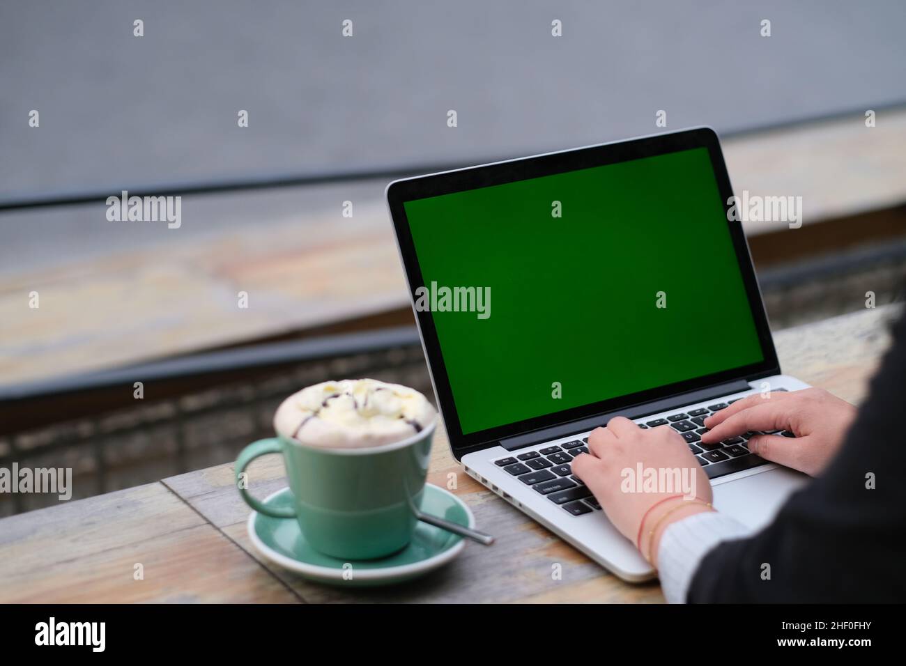 over shoulder view of hand typing on green screen laptop computer. Cup of coffee on cafe table Stock Photo