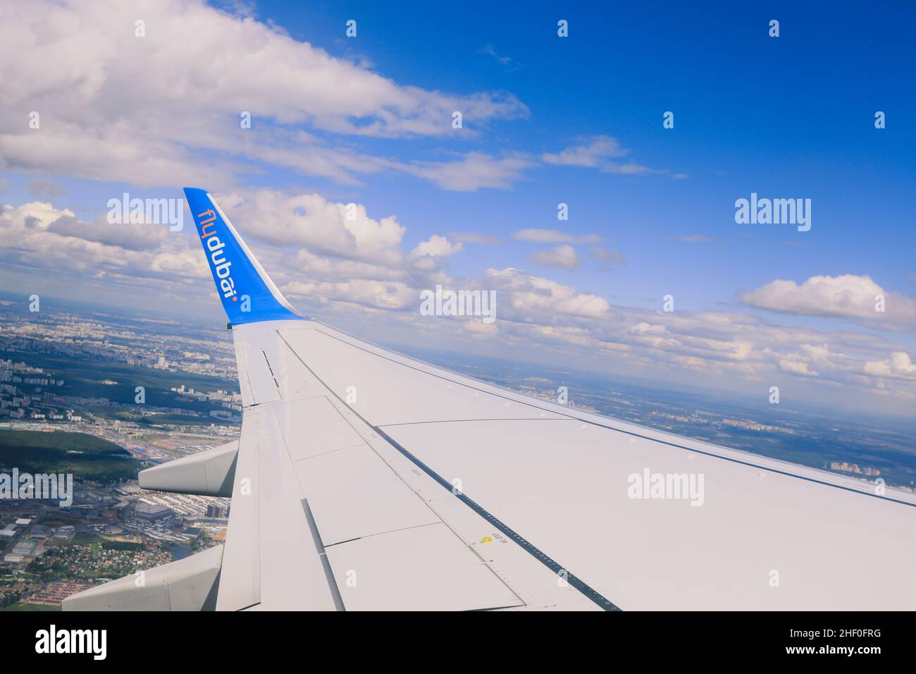 Dubai, United Arab Emirates - June 10, 2021: Window View to the Aircraft Wing and Cloudy Blue Sky Stock Photo