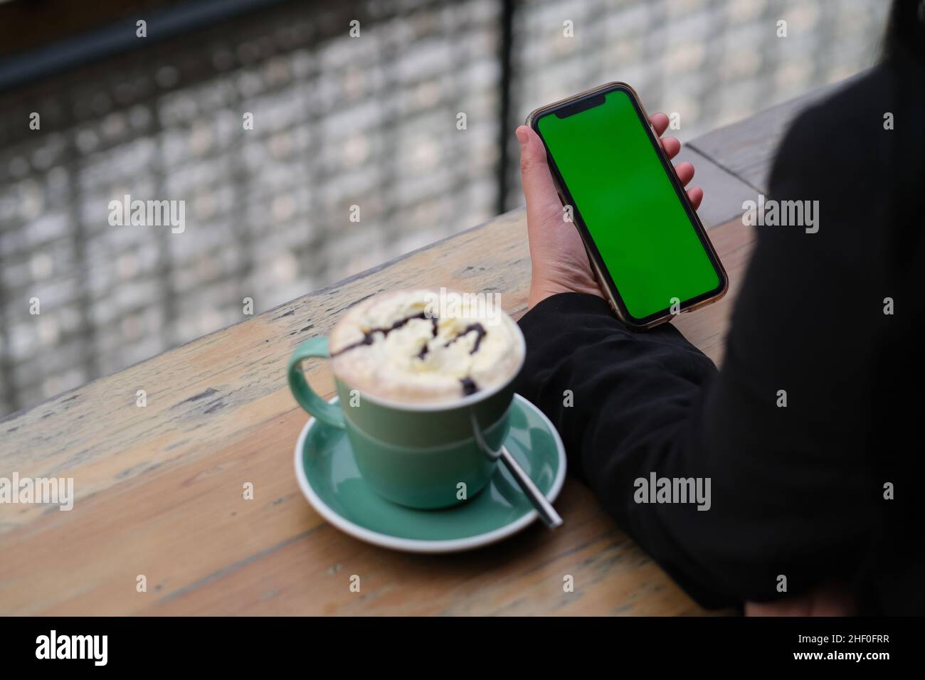 over shoulder view of hand holding green screen mobile phone. Cup of coffee on cafe table Stock Photo