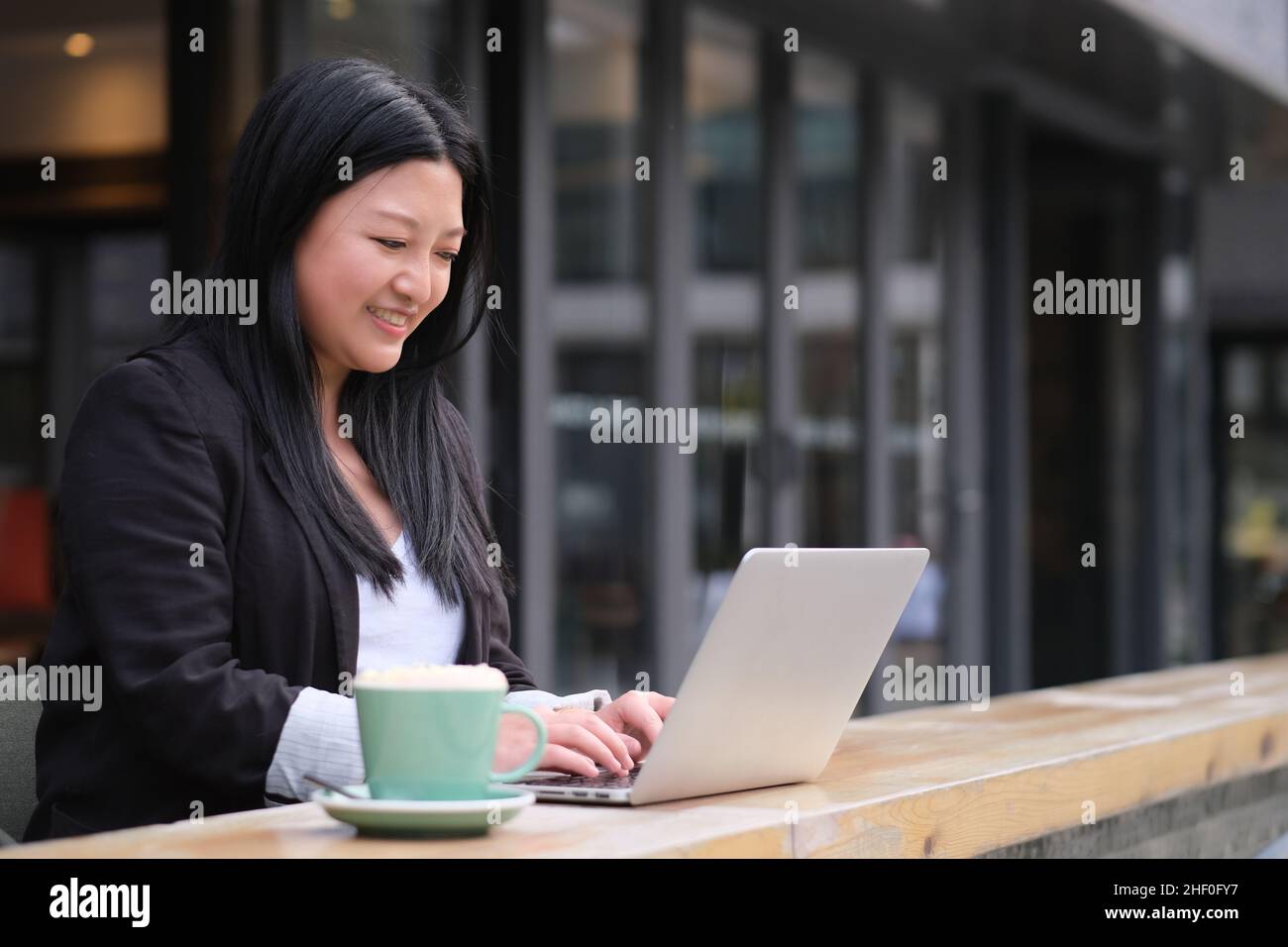portrait of smiling Asian young business woman working on laptop computer at outdoor cafe Stock Photo