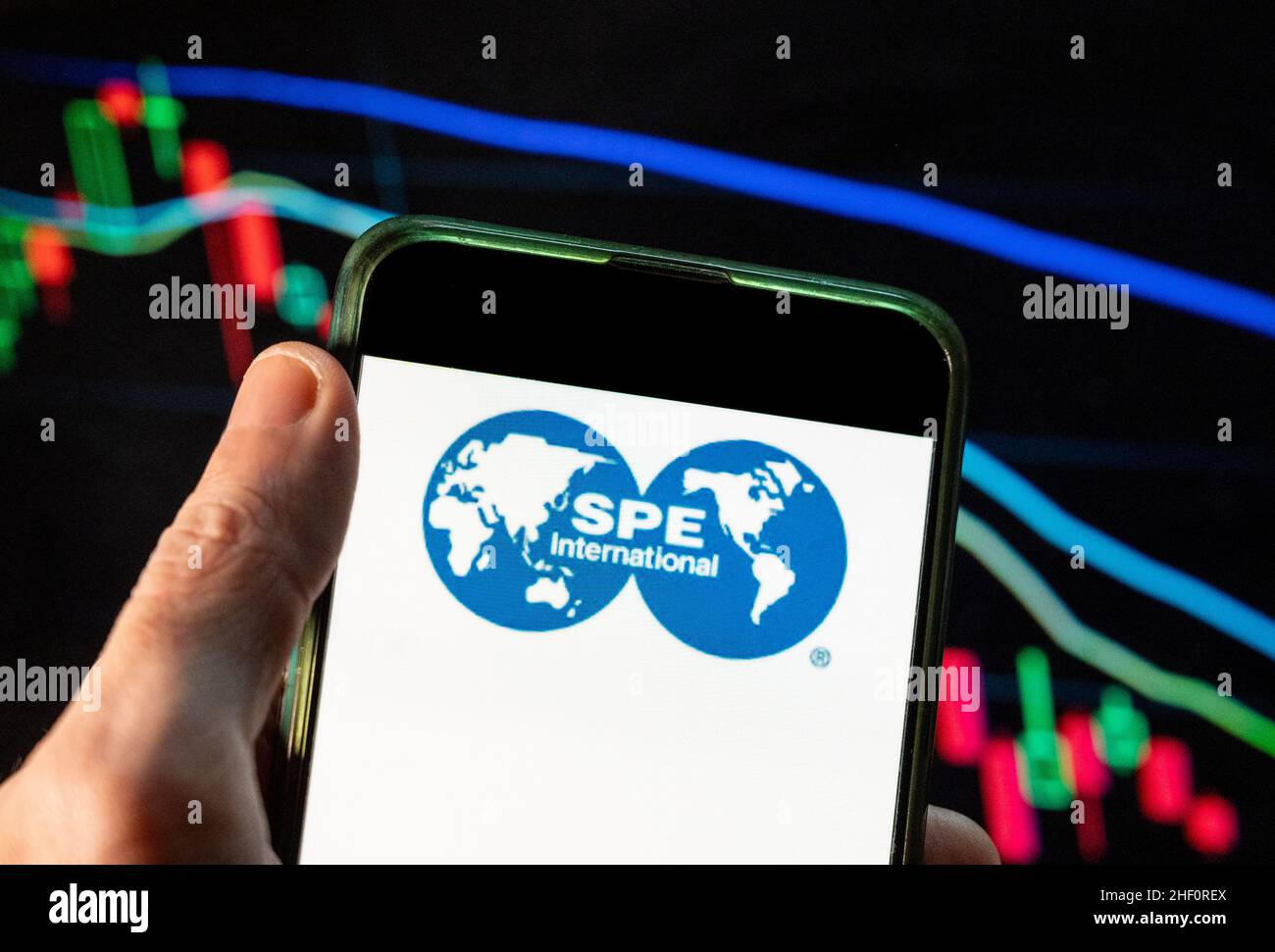 In this photo illustration the Society of Petroleum Engineers (SPE) logo seen displayed on a smartphone with an economic stock exchange index graph in the background. Stock Photo