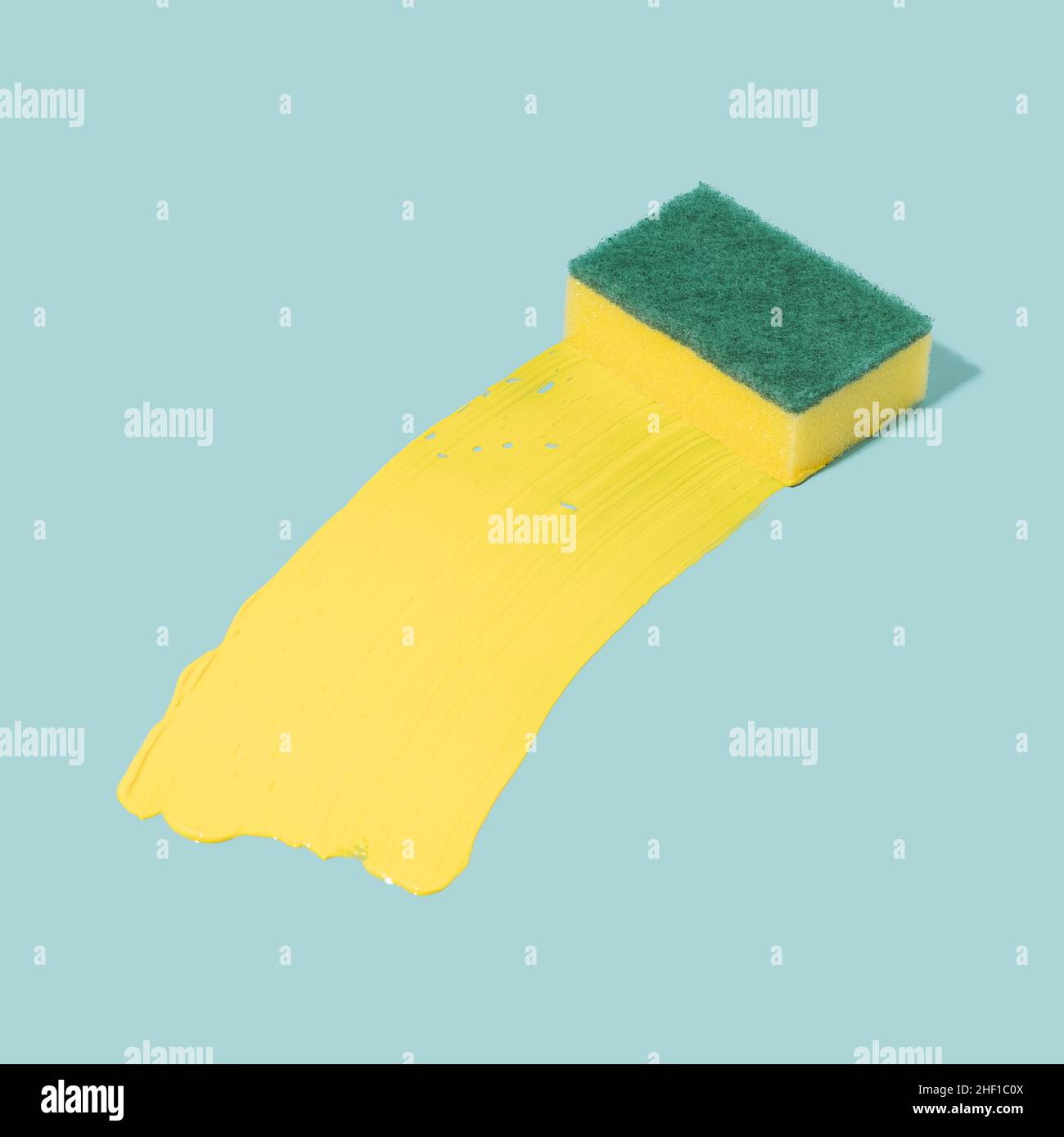 Cleaning sponge with a trail of yellow acrylic paint on a pastel blue background. Surreal cleaning concept. Stock Photo