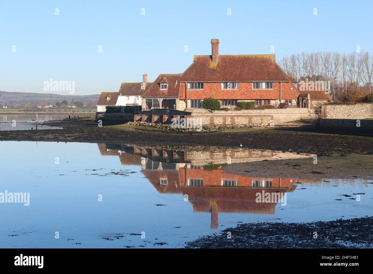 Residential building adjacent to Bosham Meadow Green with building's reflection in the water. South Downs National Park can be seen in the distance. Stock Photo