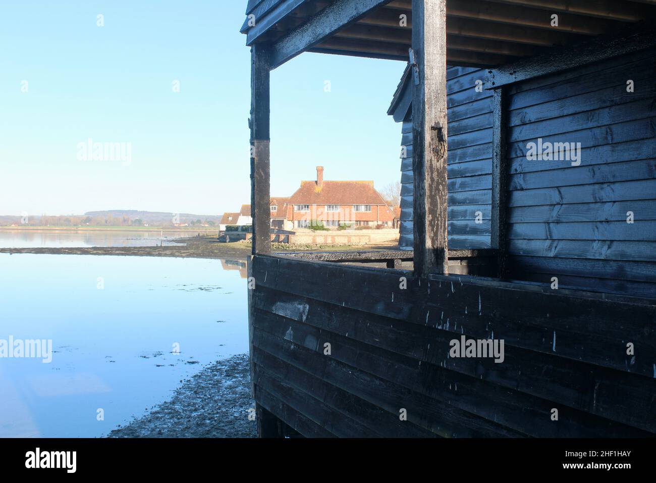 View from Bosham Quay of the ancient Raptackle former warehouse in the foreground and residential building in the background. Stock Photo