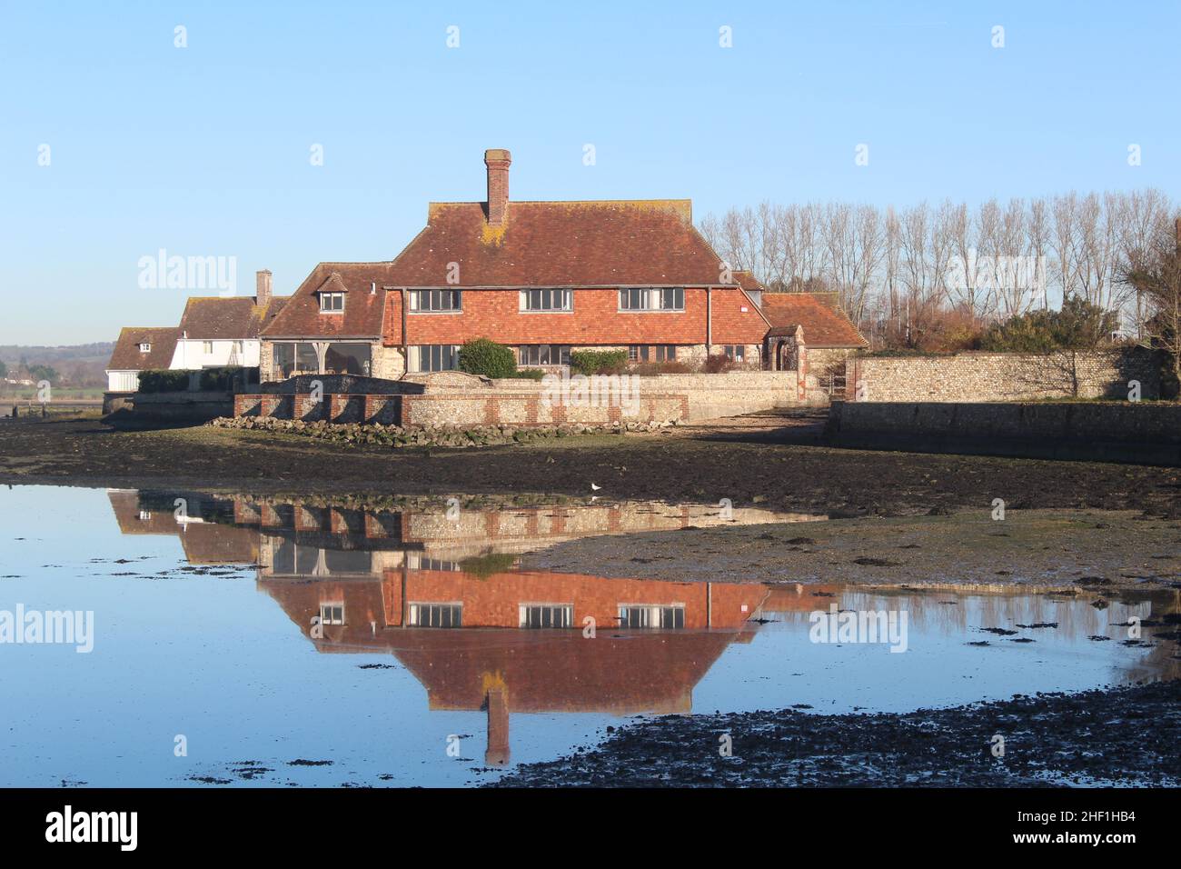Reflection of harbour-side residential property in Area of Outstanding Natural Beauty, Bosham, West Sussex. A clear blue sky on a winters day. Stock Photo