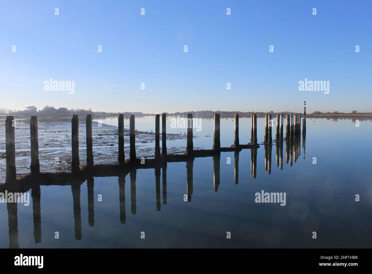 Mooring posts at Bosham Quay reflected in the still waters. Clear blue sky copy space to just add text. Stock Photo